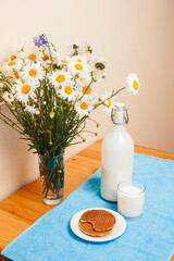 Simply stylish wooden kitchen with bottle of milk and glass on table, summer flowers camomile, healthy foog moring concept