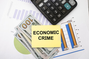 Economic crime is written on a note sheet. The sheet is on financial documents with dollars and a calculator. Business and financial concept