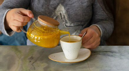 Woman holding teapot and pours healthy sea buckthorn tea into cup