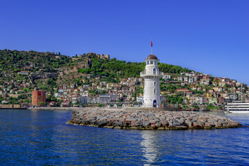 Fototapeta na wymiar Panorama of the Alanya old town (Turkey) with the Lighthouse in the middle of the Mediterranean waters. View from the sea to the coastline of the Turkish resort city