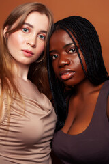 two pretty girls african and caucasian blond posing cheerful together on brown background, ethnicity diverse lifestyle people concept