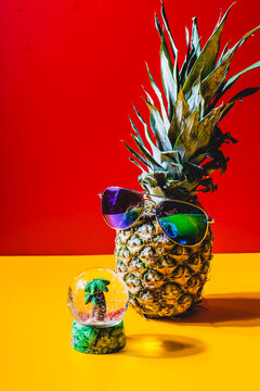 Pineapple with sunglasses in front of a snow globe with a mini palm tree