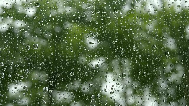 4K Droplets on glass car window in rainy day with green nature background. Concept of rain season, peace cool background.
