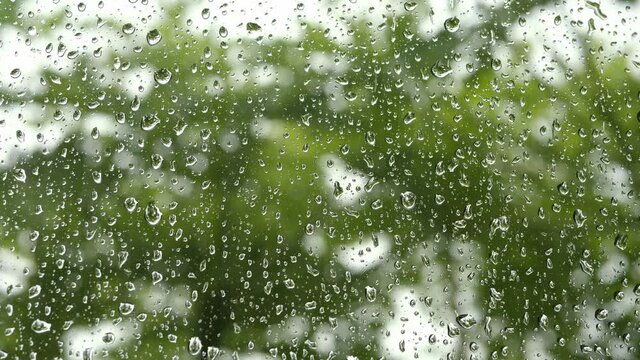 4K Droplets on glass car window in rainy day with green nature background. Concept of rain season, peace cool background.