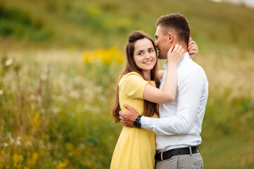 young happy couple in love hugging in a grass field in sunny day. girl in a yellow dress and a guy with a stylish haircut. portrait of couple walking on countryside