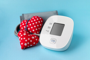 Automatic blood pressure monitor and two soft red hearts on blue background. Medical electronic...