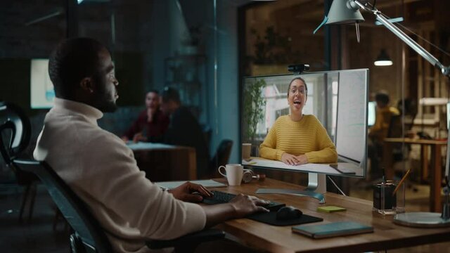 Handsome Black African American Project Manager is Making a Video Call on Desktop Computer in a Creative Office Environment. Male Specialist Talking to a Multiethnic Colleague Over a Live Camera.