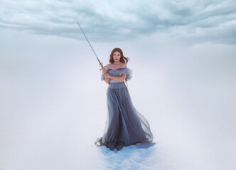 Fantasy woman princess warrior holding medieval iron sword in hands. Fairy tale snow queen. vintage gray blue dress. White winter nature background, valley, tree. Elf girl with steel blade. Art photo. © kharchenkoirina