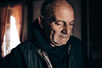 Elderly man standing by the window looking pensive, worried.