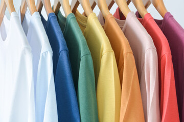 close up collection of pastel color t-shirts hanging on wooden clothes hanger in closet or clothing...