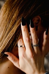 Unrecognizable vertical close up woman hand with black nail polish touching neck and earrings. Beauty concept.