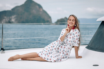 portrait of happy pretty girl with white dress and long curly blonde hair lying on yacht at summertime. looking at camera with toothy smile.