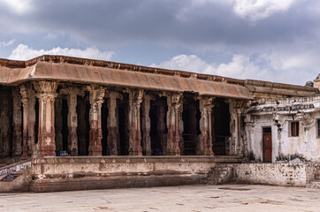 Hampi, Karnataka, India - November 4, 2013: Virupaksha Temple complex. Ruined open pillared hall in beige and dark brown stone under blue cloudscape.
