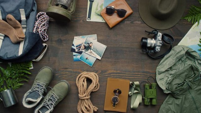 Top view flat lay shot of travel gear and accessories lying on wooden table. Unrecognizable woman putting photos from recent trips in center