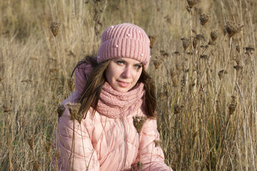 A girl in autumn clothes among the dried tall grass. Walking in nature in the park.