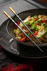 Asian noodles. Noodles with mushrooms and vegetables. Food sticks. Plate with noodles on a dark background.