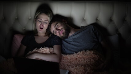 Naklejka premium Man and woman, young couple watching boring movie on laptop in bed before bedtime