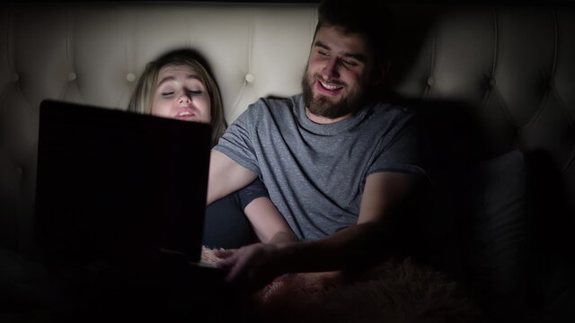 A man and a woman, a young couple watching a movie in bed before going to bed and cannot share a laptop
