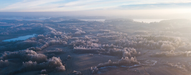 Aerial view from above of a countryside landscape with beautiful sunset light on a winter evening with forzen meadows and mist hazy horizon, banner