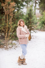 Beautiful young woman in jeans and pink jacket in winter forest
