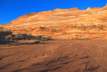 Fototapeta na wymiar The Wave area after flash flood. A cliff of sand dune layers turned to rock with water swirly lines in wash seemed to compliment each other. Arizona, USA