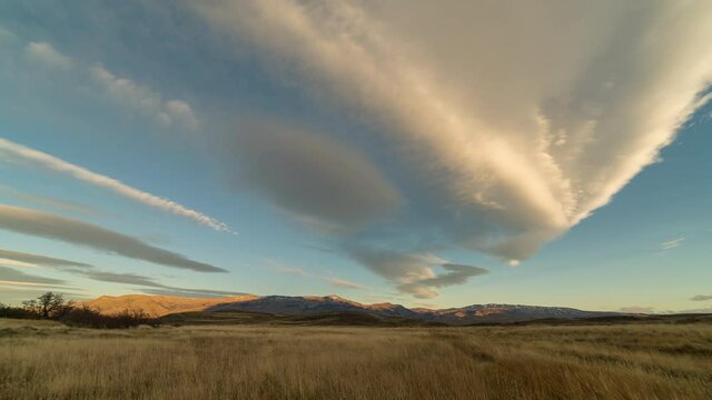 Time lapse of the clouds moving  across a grassland in the National Park Torres del Paine with mountains on the horizon, evening sunlight.