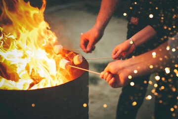Human hands holding sticks for open fire marshmallow roasting at night time. Close view background...