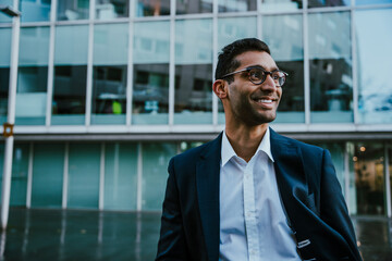 Middle-aged businessman wearing spectacles smiling standing outside banking office building