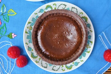 Overhead view of a chocolate coulant on a blue  tablecloth surrounded raspberries