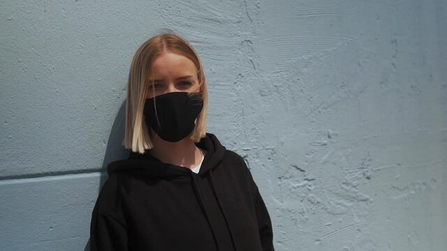 New Normal. Girl With Face Mask by The Wall, Blonde Hair on Summer Breeze, Slow Motion. Covid-19 Virus Pandemic Outbreak, Quarantine and Lockdown Concept