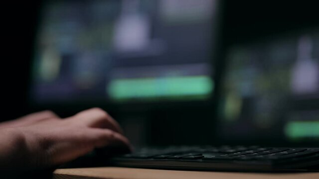 Male hands typing on keyboard, defocused monitors deen on background, hacker breaking firewall