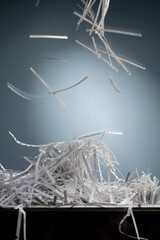 A pile of shredded paper strips lie in a metal box and from above, more strips fall down with motion blur.