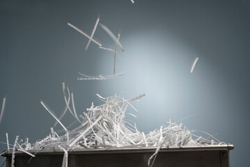 A pile of shredded paper strips lie in a metal box and from above, more strips fall down with motion blur.