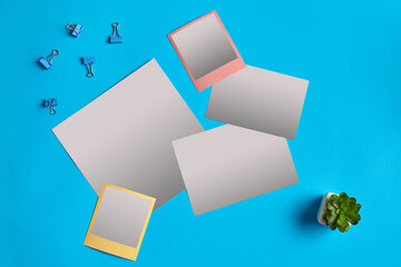 Empty white sheets of paper, colorful blank reminders, binder clips and green succulent in a pot on blue background. Close up, copy space