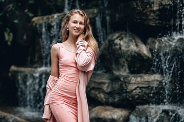 Young woman in pink dress  posing near blurred waterfall. Kuala Lumpur. Malaysia.