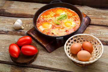 israeli fried eggs with cheese in a frying pan near products on a wooden table