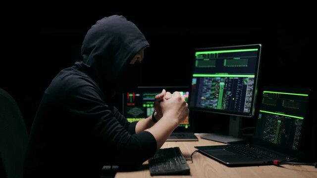 Criminal in mask hood typing fast on keyboard, cyber attack on security systems, fraud