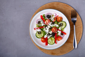 Light plate of Greek salad on a round shelf with a fork on a concrete background.