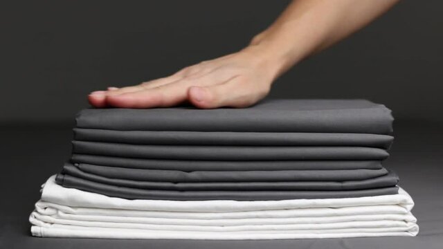 The woman's hands smooth out a stack of folded sheets and place a pink feather on top of it.