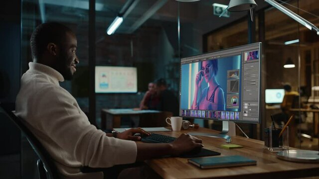 Handsome Black African American Specialist Working on Desktop Computer in Creative Office Environment. Hipster Male is Editing a Fashion Photograph with Model in a Digital Graphics Editing Software.