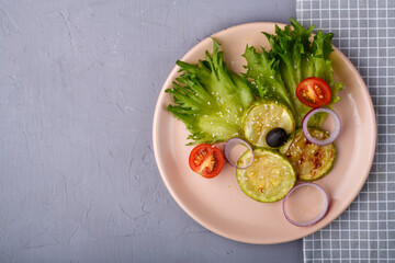 Light plate of greek salad near a napkin on a gray concrete background. Copy space.
