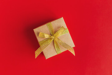 Gift box with golden ribbon on a red background with gold glitter.
