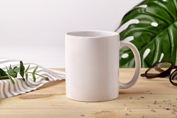 Ceramic mug on wooden desktop next to striped tablecloth, scattered crystals and green plants on...