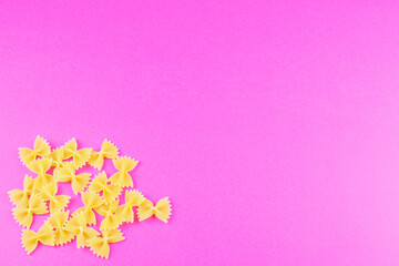 farfalle spread out in the corner on a bright pink background. Pasta pattern.