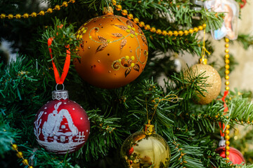 Fototapeta na wymiar Yellow Christmas ball hanging on a Christmas tree against the backdrop of a glowing garland