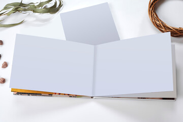 Open photo book with blank pages, empty sheet of paper, green twig and small stones isolated on...