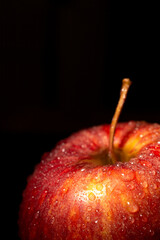 Top of red apple with water drops, illuminated, with selective focus, black background, vertical, with copy space