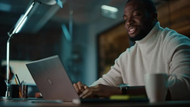 Handsome Black African American Man Having an Online Video Call on a Laptop Computer in Creative Office Environment. Happy Project Manager Talking to Colleague About Business Strategy.