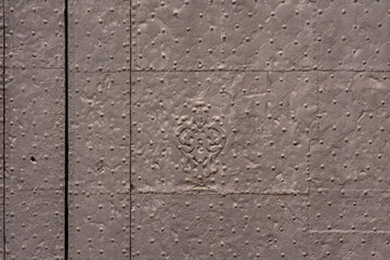 Old metal panel with edging and nails forming patterns and figures, on an old door. Grey background
