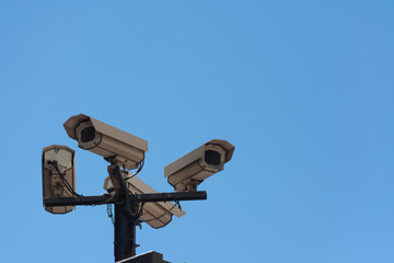 Four security cameras on a pole in the street, from below, with a blue sky. Concepts like security or privacy